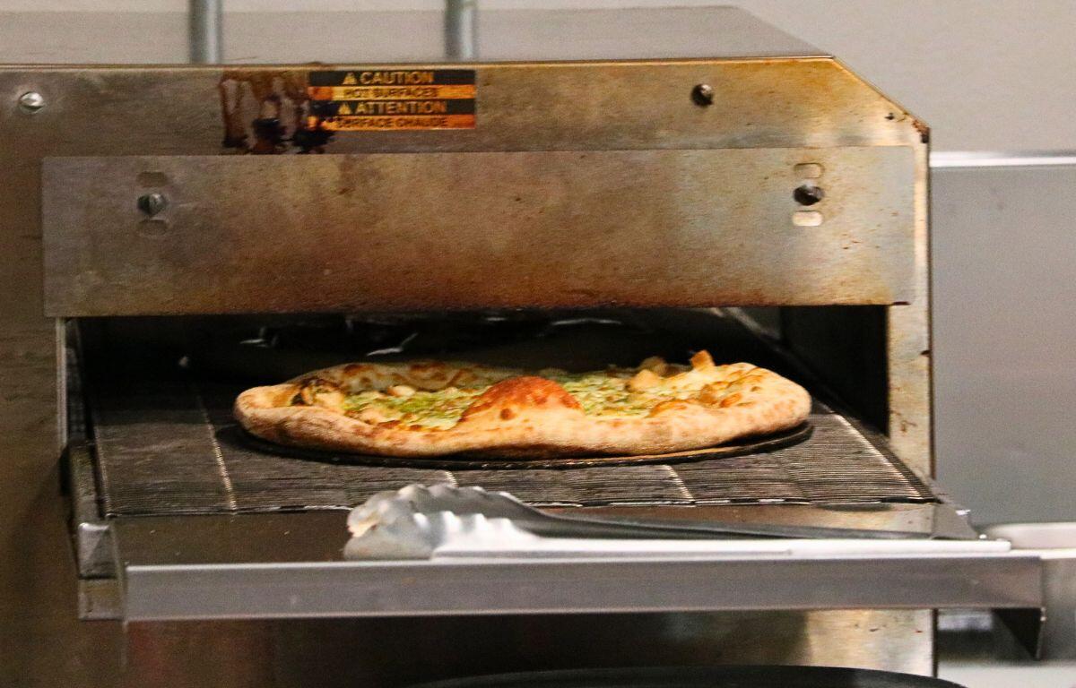 Pizza baking inside a large industrial oven on a metal rack with tongs resting in front of it.