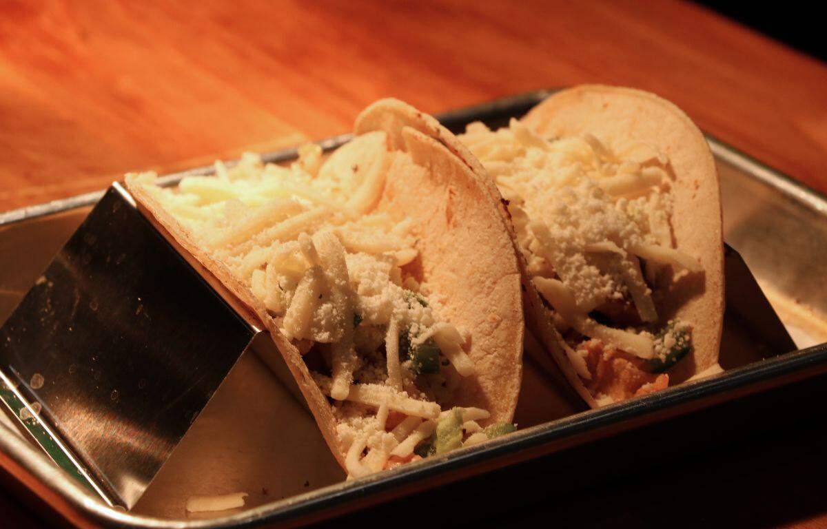Two soft tacos opened to reveal shredded cheese and vegetables on a metal tray.