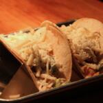 Two soft tacos opened to reveal shredded cheese and vegetables on a metal tray.