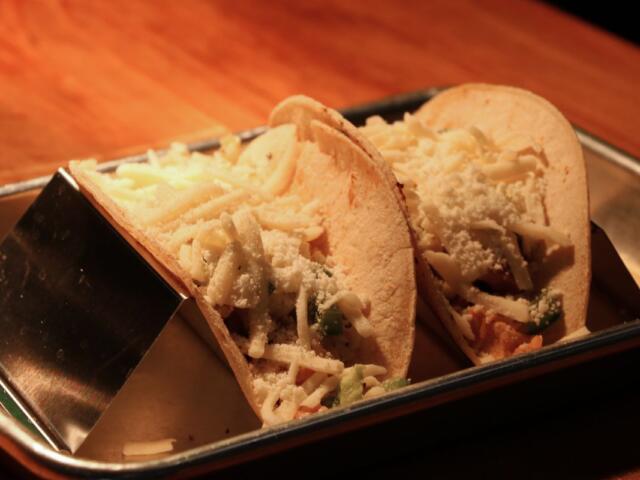 Two soft tacos opened to reveal shredded cheese and vegetables on a metal tray.