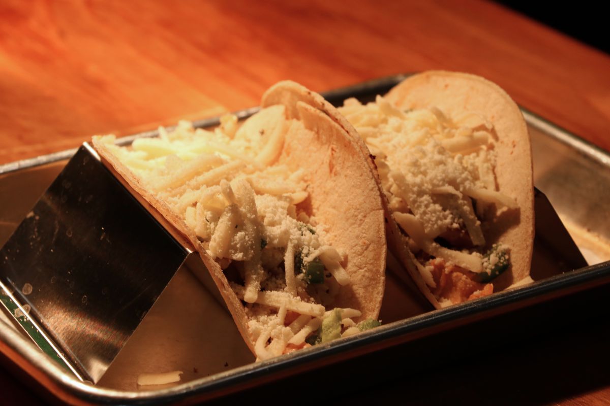 Two soft tacos opened to reveal shredded cheese and vegetables on a metal tray.