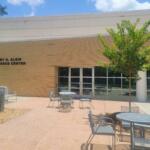 Brick exterior of Marvey R. Klein Conference Center with a tree, metal tables and chairs in a sunny courtyard.