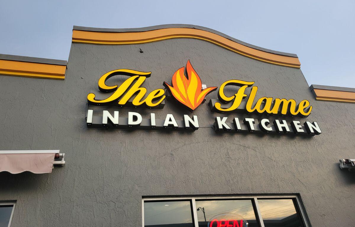 A gray building facade with a sign that reads, "The Flame Indian Kitchen."