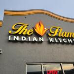 A gray building facade with a sign that reads, "The Flame Indian Kitchen."