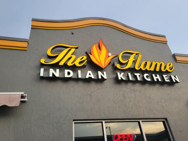 A gray building facade with a sign that reads, "The Flame Indian Kitchen."