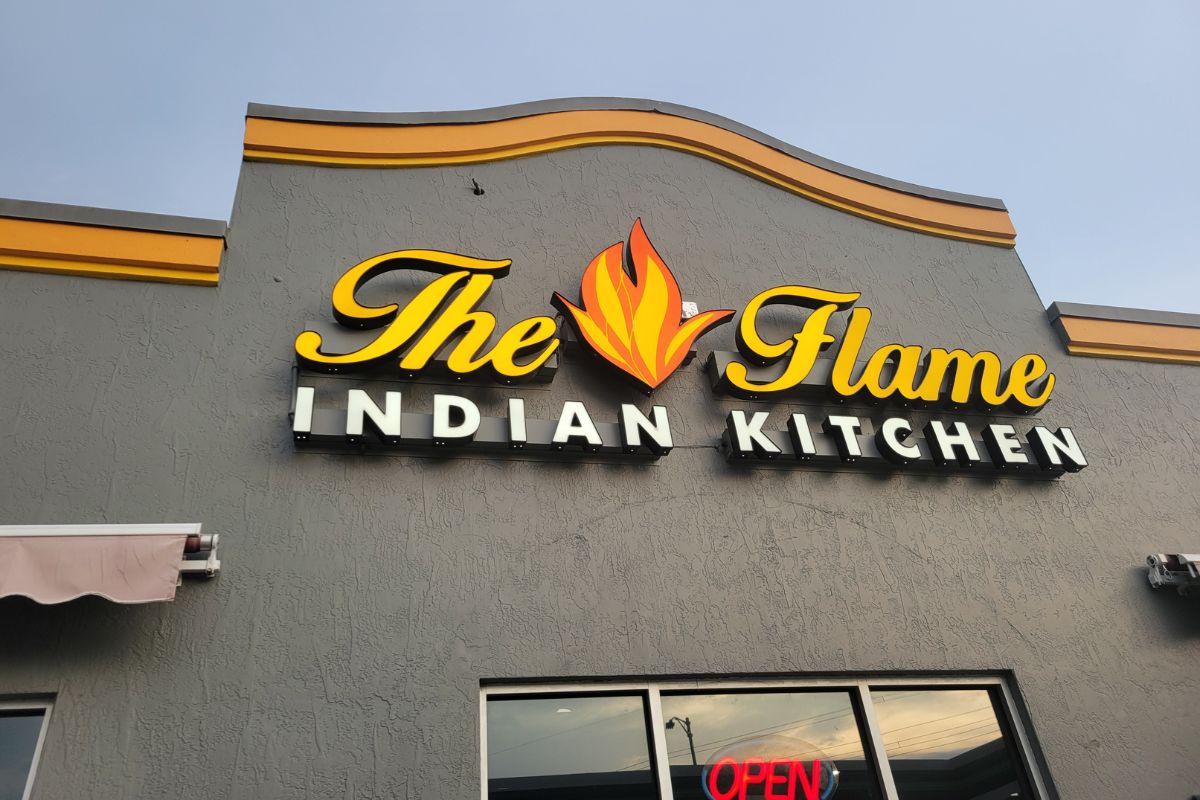 A gray building facade with a sign that reads, "The Flame Indian Kitchen."