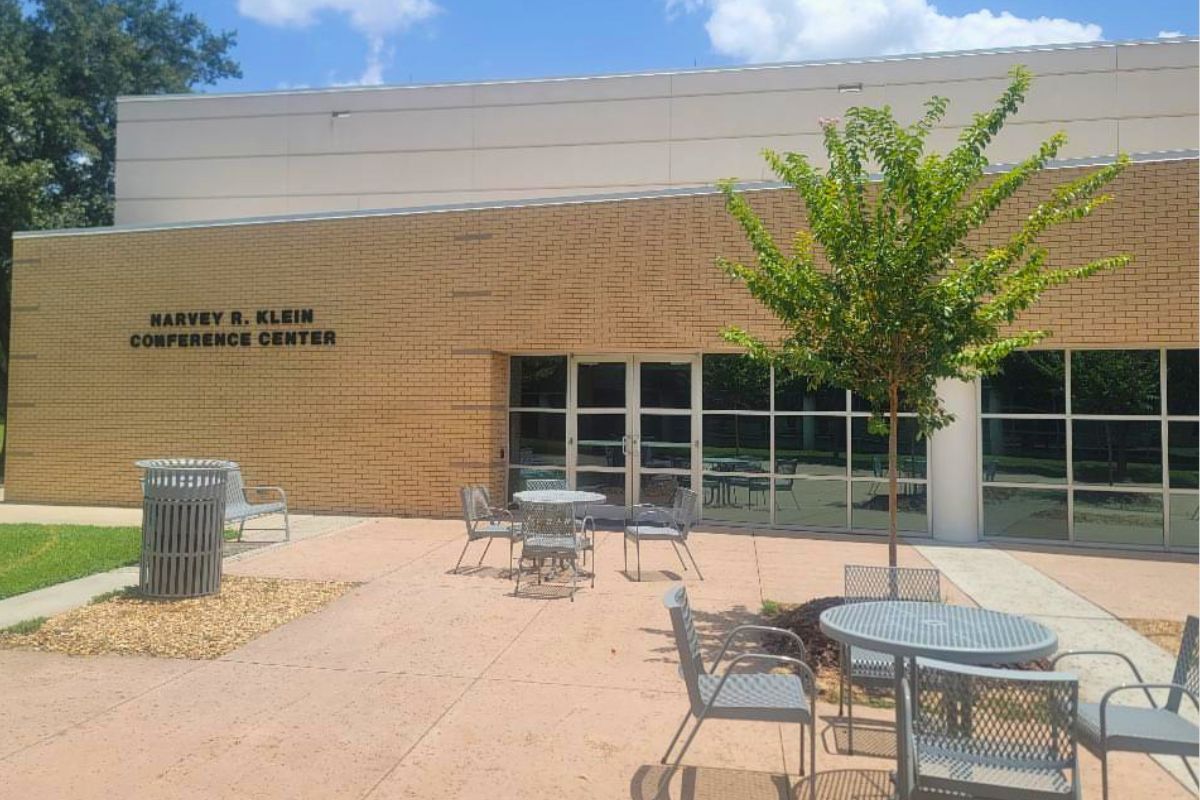 Brick exterior of Marvey R. Klein Conference Center with a tree, metal tables and chairs in a sunny courtyard.