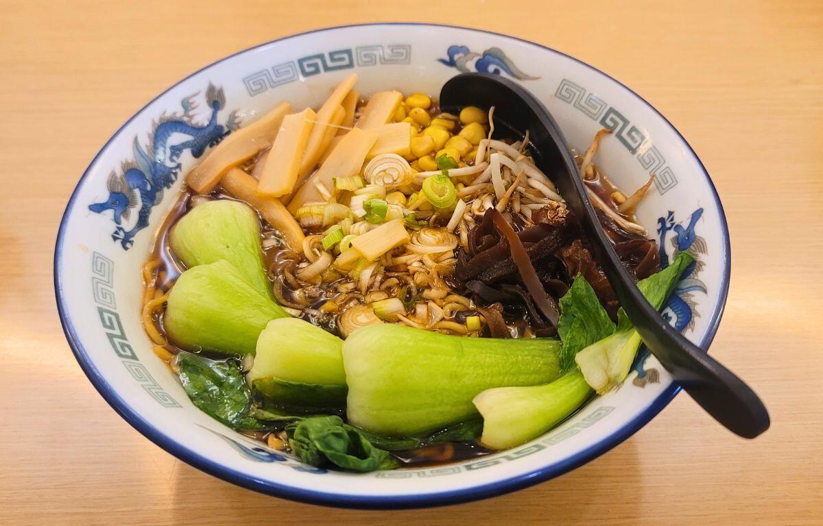 A bowl of ramen filled with vegetables on a table.