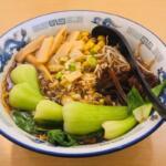 A bowl of ramen filled with vegetables on a table.