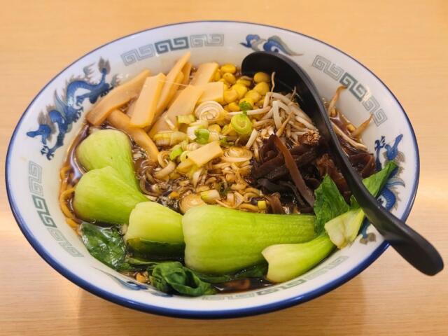A bowl of ramen filled with vegetables on a table.