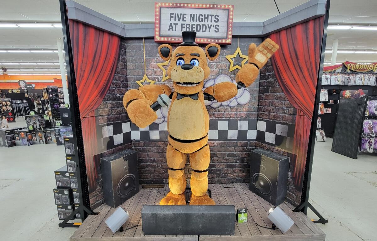 A plush bear animatronic with a bowtie and hat waving.