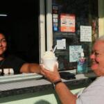 A restaurant window exterior. Woman hands another woman ice cream in a cup through a window.