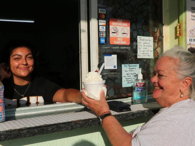 A restaurant window exterior. Woman hands another woman ice cream in a cup through a window.