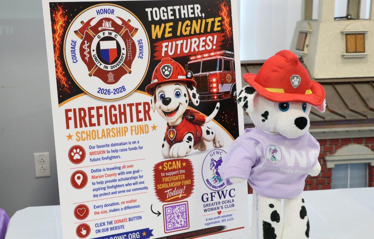 A dalmatian plush toy on a white table. A sign advertising a firefighter scholarship fund behind it.