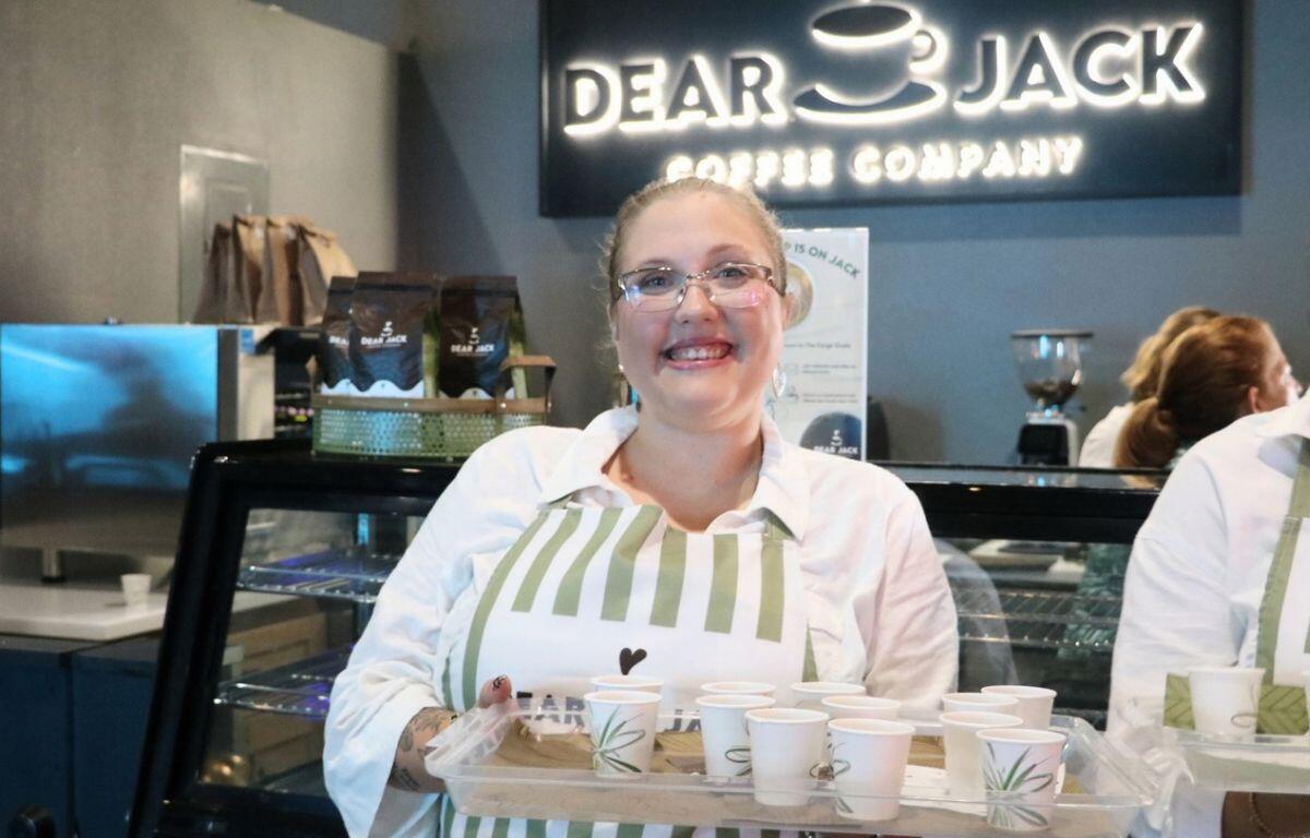 Woman holds sample cups with coffee in front of coffee shop. A sign reads, "Dear Jack Coffee Company."
