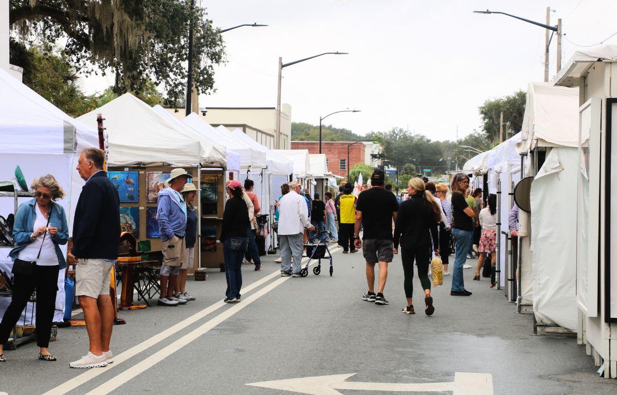 Crowd of people walk through white canopies lined up on a street.