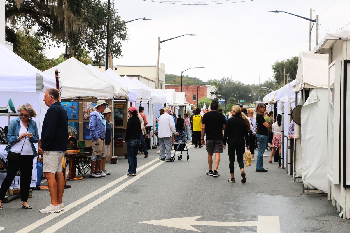 Crowd of people walk through white canopies lined up on a street.