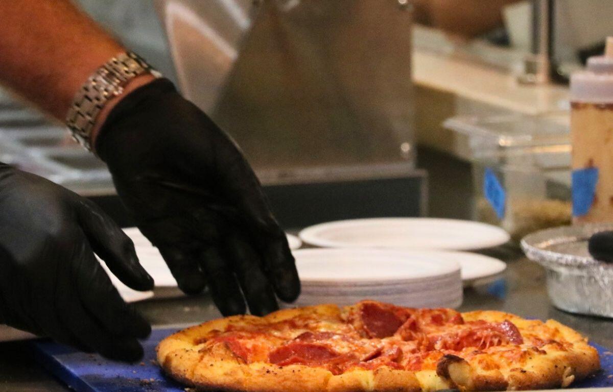 Pizza being divided into slices in restaurant kitchen.