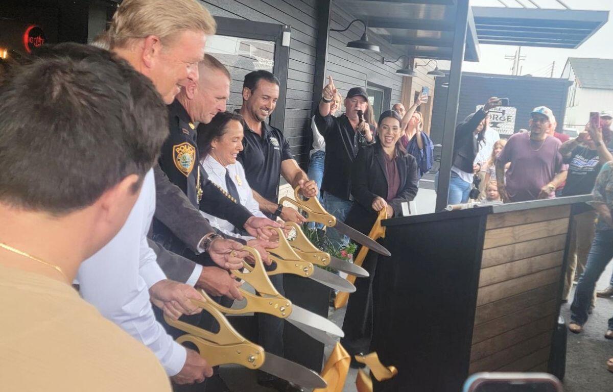 A line of people cut a ribbon with large scissors while a crowd watches.